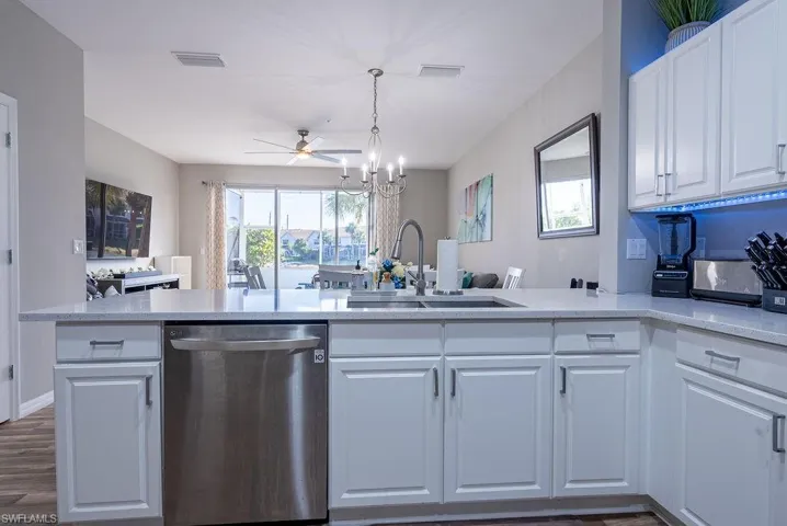 Kitchen with open floor plan, dishwasher, white cabinets, light stone counters, and ceiling fan