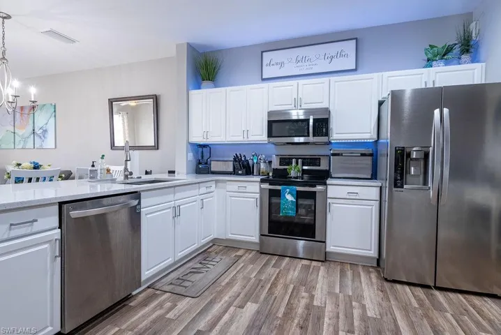 Kitchen featuring appliances with stainless steel finishes, white cabinets, light wood-style floors, pendant lighting, and light stone countertops