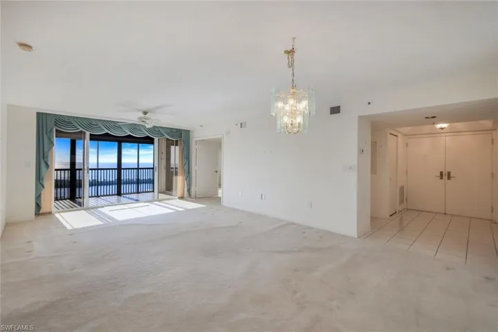 Spare room with ceiling fan with notable chandelier and light colored carpet