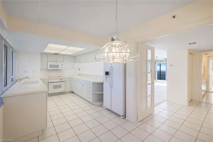 Kitchen featuring white appliances, decorative light fixtures, white cabinetry, and sink