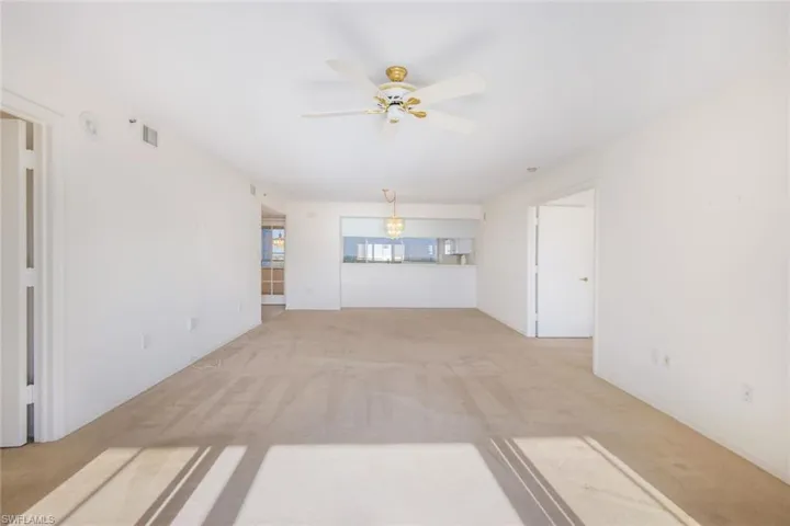 Unfurnished living room featuring ceiling fan with notable chandelier and light carpet