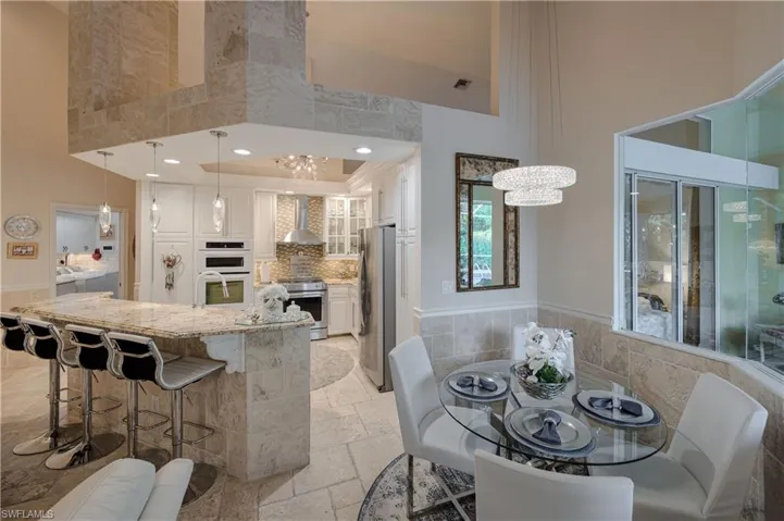 Kitchen featuring decorative light fixtures, white cabinets, a high ceiling, stainless steel appliances, and wall chimney exhaust hood