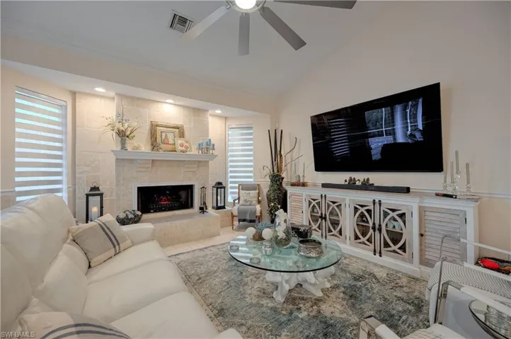 Living room with a tile fireplace, lofted ceiling, ceiling fan, and crown molding