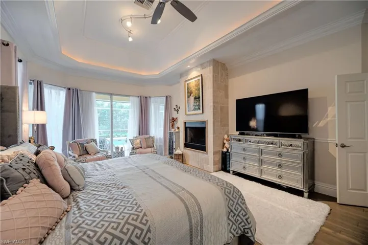 Bedroom featuring crown molding, hardwood / wood-style flooring, a tile fireplace, access to exterior, and a raised ceiling
