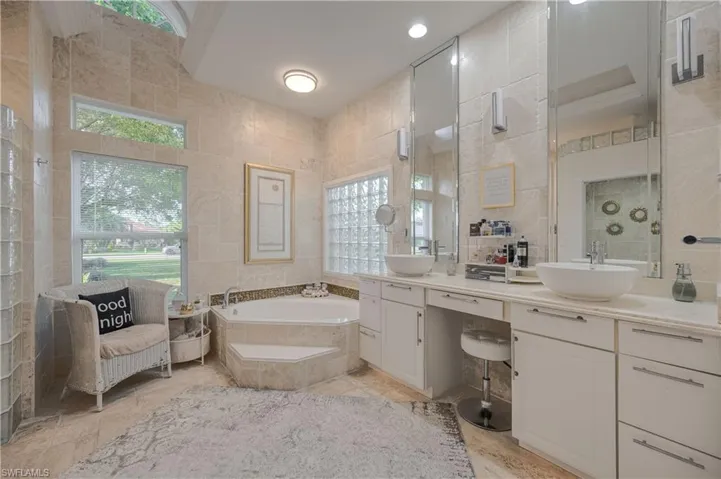 Bathroom with tile walls, vanity, plenty of natural light, and tiled bath