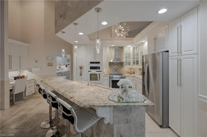 Kitchen with a large island, stainless steel appliances, white cabinets, decorative light fixtures, and wall chimney exhaust hood