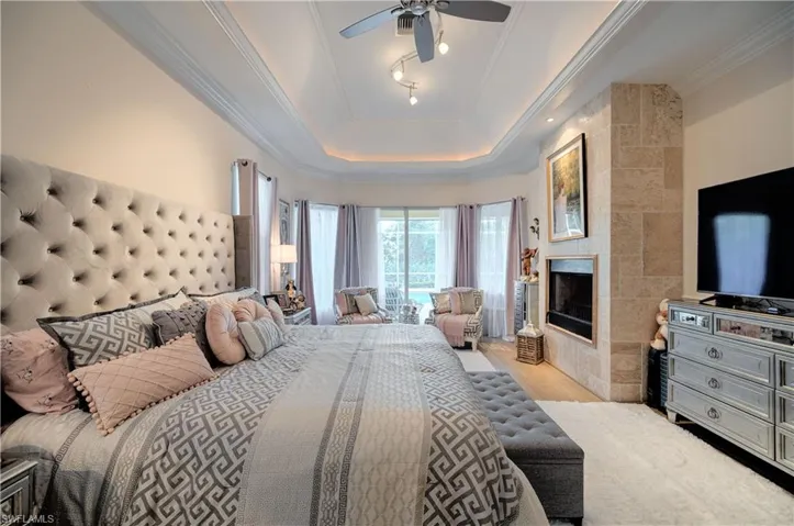 Bedroom featuring crown molding, a fireplace, a raised ceiling, and light wood-type flooring