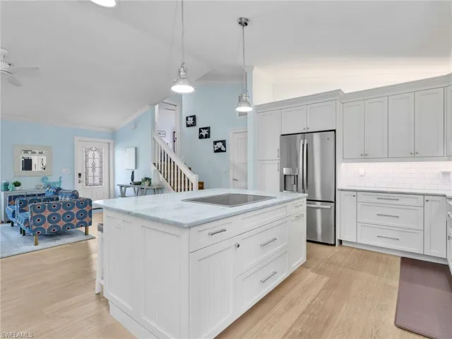 Kitchen featuring vaulted ceiling, stainless steel fridge, crown molding, white cabinetry, and open floor plan