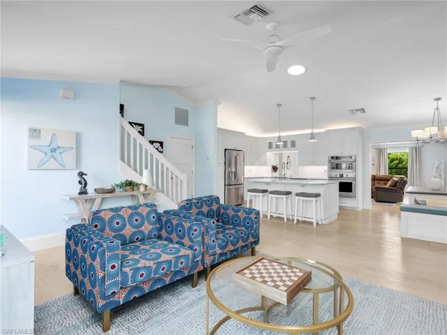 Living area featuring ceiling fan, lofted ceiling, a chandelier, light wood finished floors, and stairs