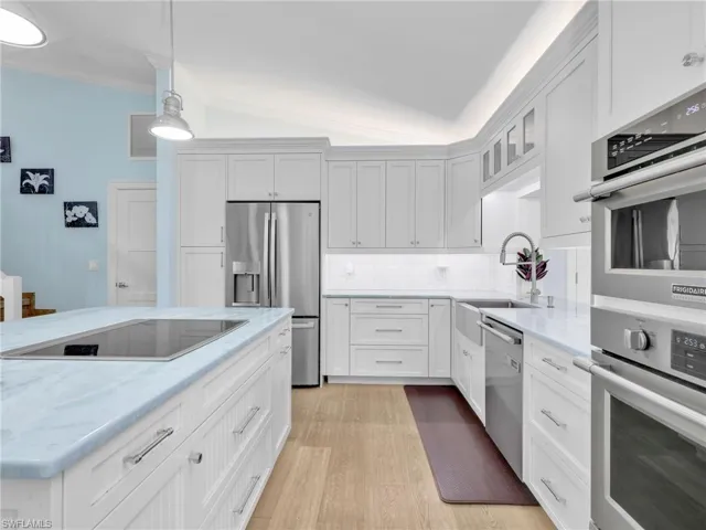 Kitchen with lofted ceiling, stainless steel appliances, white cabinets, hanging light fixtures, and light stone counters