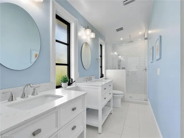 Full bath with a shower stall, two vanities, light tile patterned flooring, and recessed lighting