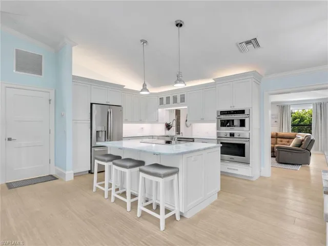 Kitchen featuring vaulted ceiling, a breakfast bar, appliances with stainless steel finishes, crown molding, and decorative light fixtures