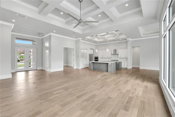 Unfurnished living room with french doors, coffered ceiling, a towering ceiling, light wood-style flooring, and a ceiling fan