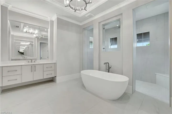 Bathroom with vanity, a walk in shower, a chandelier, a soaking tub, and crown molding