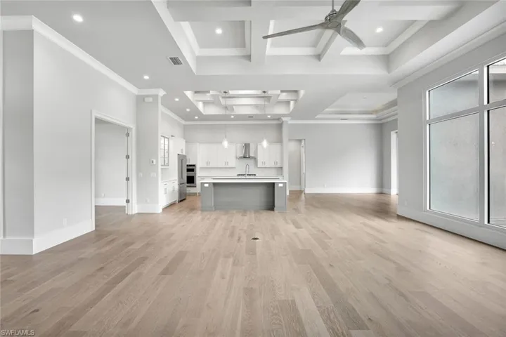 Unfurnished living room with crown molding, coffered ceiling, recessed lighting, light wood finished floors, and ceiling fan