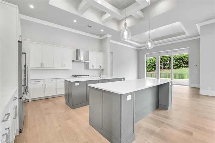 Kitchen featuring white cabinetry, ornamental molding, hanging light fixtures, coffered ceiling, and light wood-style floors