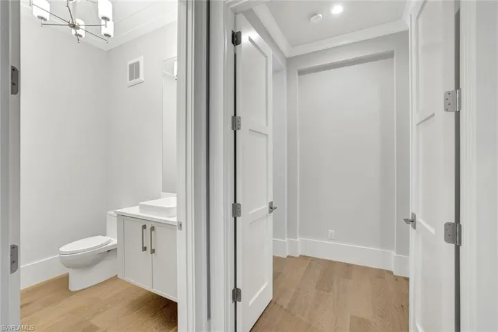 Half bathroom with vanity, light wood-style floors, crown molding, and a chandelier