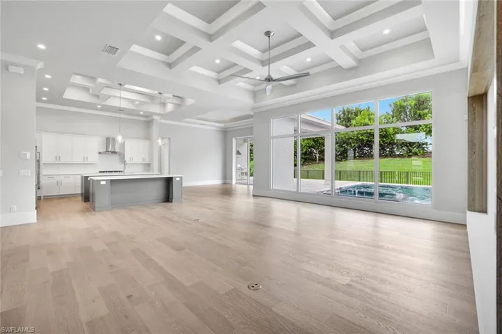 Unfurnished living room featuring ceiling fan, coffered ceiling, ornamental molding, light wood-style flooring, and beam ceiling