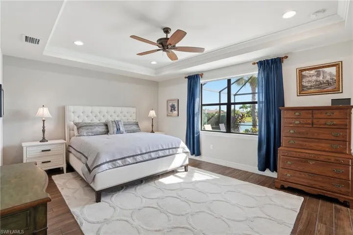 Bedroom with a raised ceiling, recessed lighting, dark wood-type flooring, ornamental molding, and ceiling fan