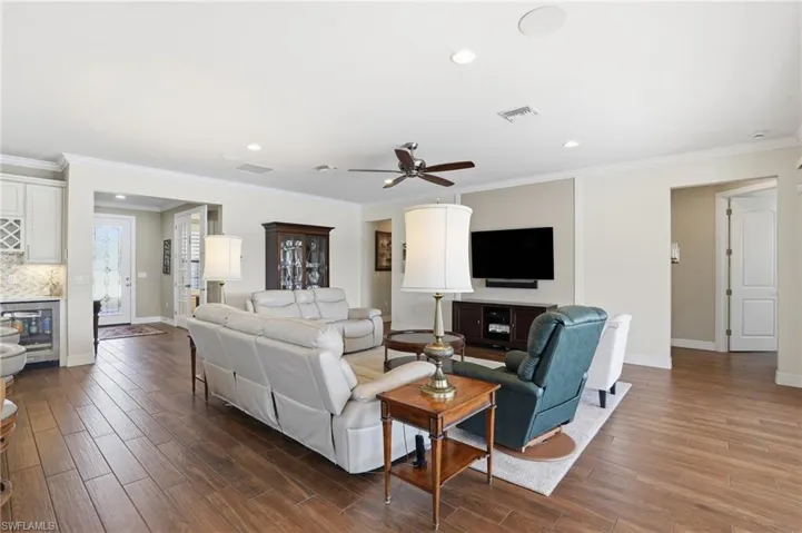 Living room with ornamental molding, dark wood-style floors, beverage cooler, recessed lighting, and ceiling fan