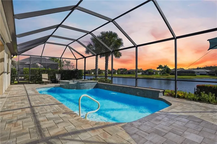 Pool at dusk with a sunroom, a pool with connected hot tub, a lanai, a water view, and a patio area