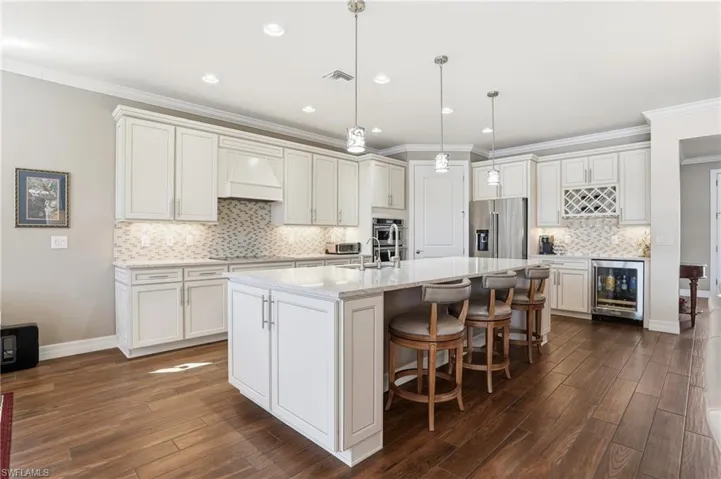 Kitchen with ornamental molding, pendant lighting, appliances with stainless steel finishes, a kitchen bar, and a kitchen island with sink