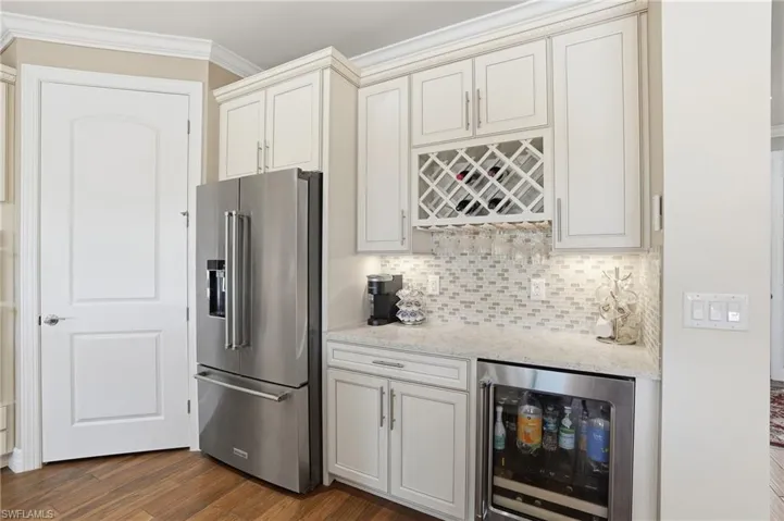 Kitchen with high end refrigerator, light stone countertops, wine cooler, backsplash, and dark wood-type flooring
