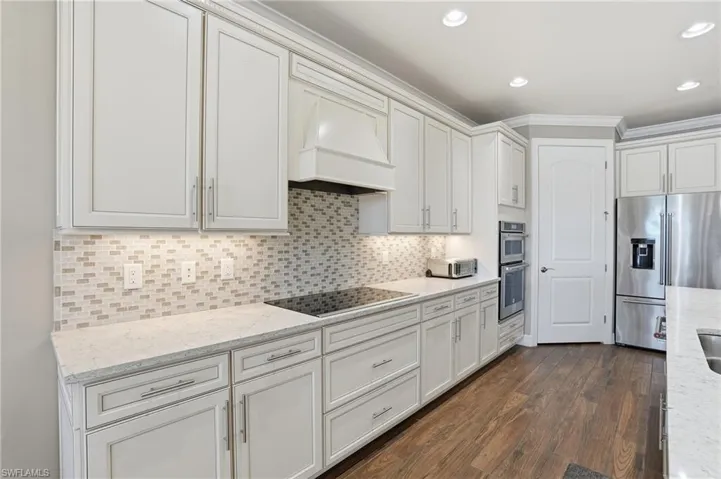 Kitchen with stainless steel appliances, light stone countertops, decorative backsplash, dark wood finished floors, and recessed lighting
