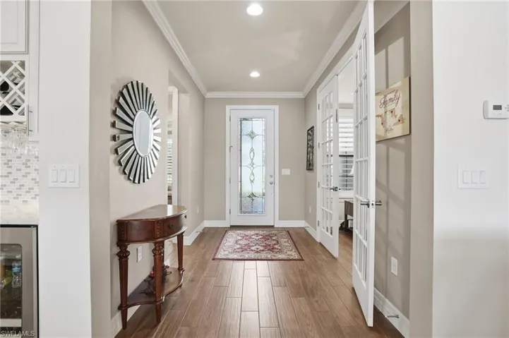 Entrance foyer featuring french doors, ornamental molding, beverage cooler, wood finished floors, and recessed lighting