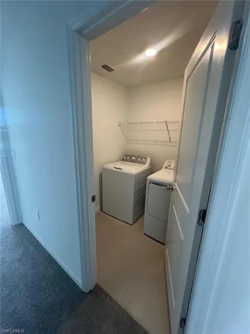 Laundry room with separate washer and dryer, light colored carpet, and light tile patterned floors