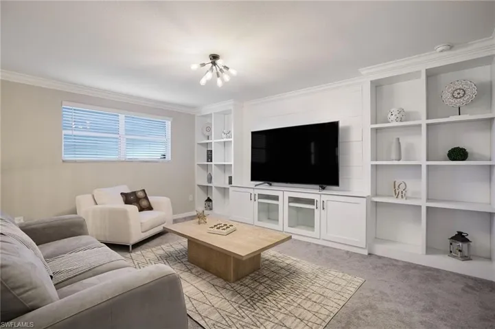 Living room with crown molding, a chandelier, and light colored carpet