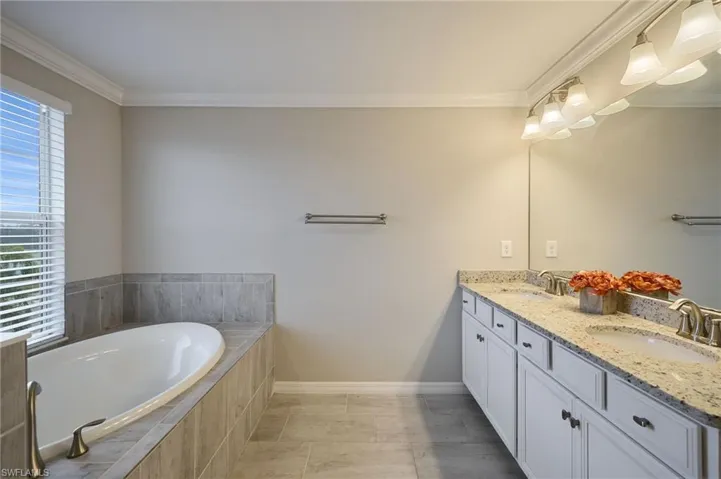 Bathroom with tiled bath, vanity, ornamental molding, and tile patterned flooring