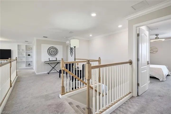 Hallway with built in features, light colored carpet, and crown molding