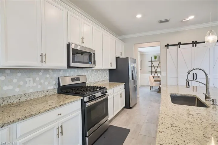 Kitchen with decorative backsplash, sink, white cabinetry, and stainless steel appliances
