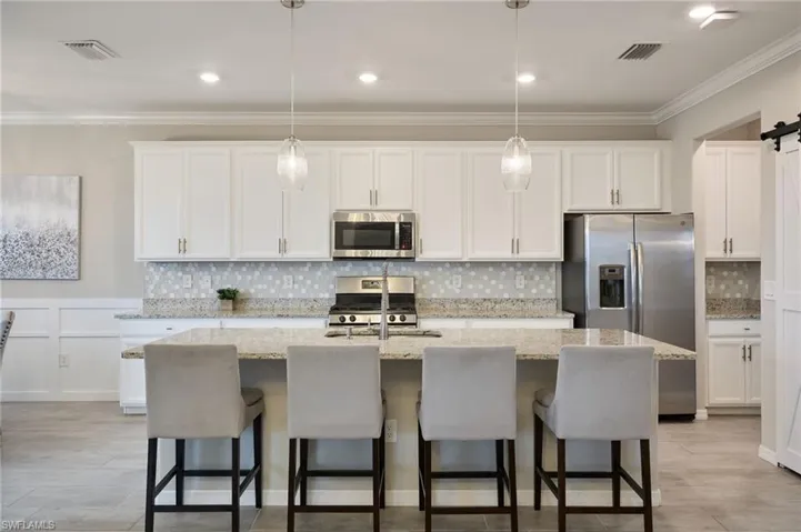 Kitchen with an island with sink, white cabinets, pendant lighting, and stainless steel appliances