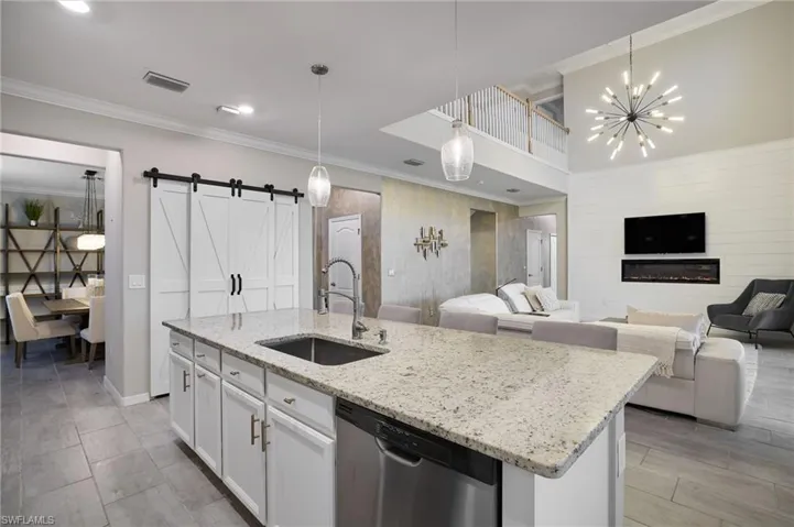 Kitchen featuring a barn door, stainless steel dishwasher, sink, white cabinets, and pendant lighting