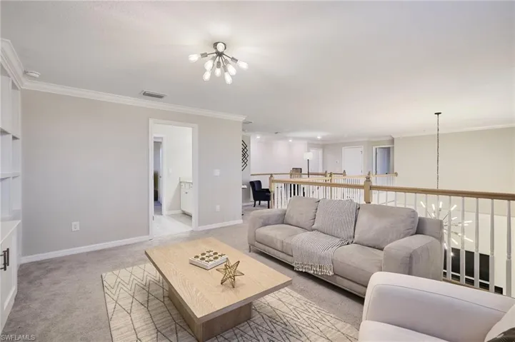Carpeted living room featuring crown molding and a notable chandelier