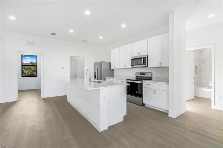 Kitchen with white cabinetry, appliances with stainless steel finishes, light hardwood / wood-style flooring, and an island with sink