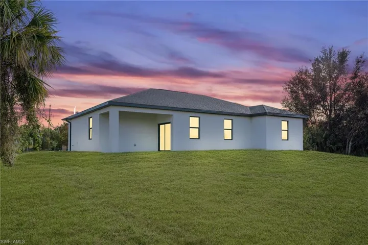 Back house at dusk featuring a lawn