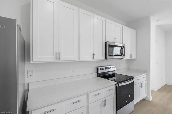Kitchen featuring light stone countertops, appliances with stainless steel finishes, white cabinetry, and light wood-type flooring