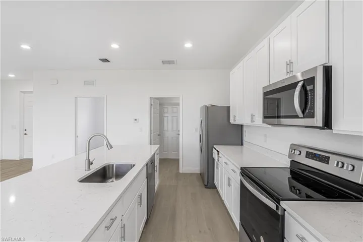 Kitchen featuring light hardwood / wood-style flooring, stainless steel appliances, sink, light stone countertops, and white cabinetry