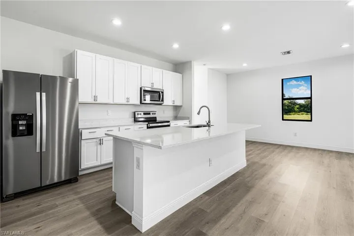 Kitchen with wood-type flooring, sink, an island with sink, stainless steel appliances, and white cabinets