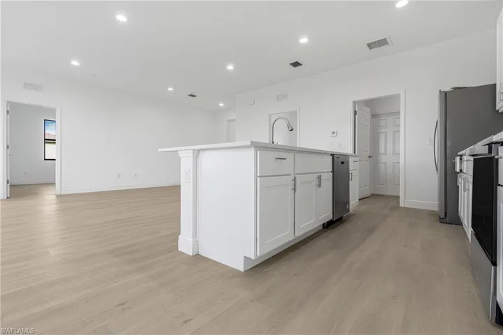 Kitchen featuring light hardwood / wood-style floors, white cabinetry, and a kitchen island with sink