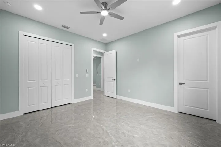 Spacious room featuring light blue walls, gray polished tile flooring, a ceiling fan with integrated lighting, recessed lighting, and white bi-fold closet doors