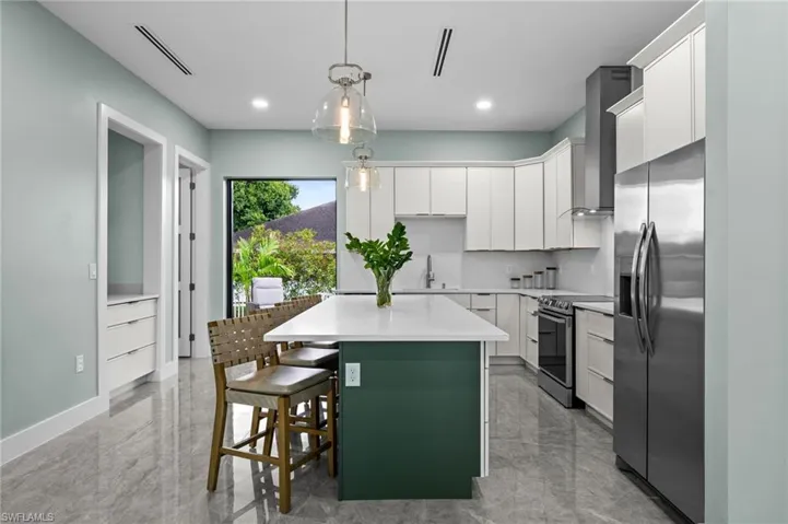 Modern kitchen featuring a central island with seating, white cabinetry, stainless steel appliances, and large format tile flooring