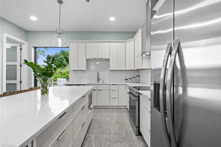 Modern kitchen featuring a large center island with a white countertop, extensive white cabinetry, stainless steel appliances, and grey tile flooring