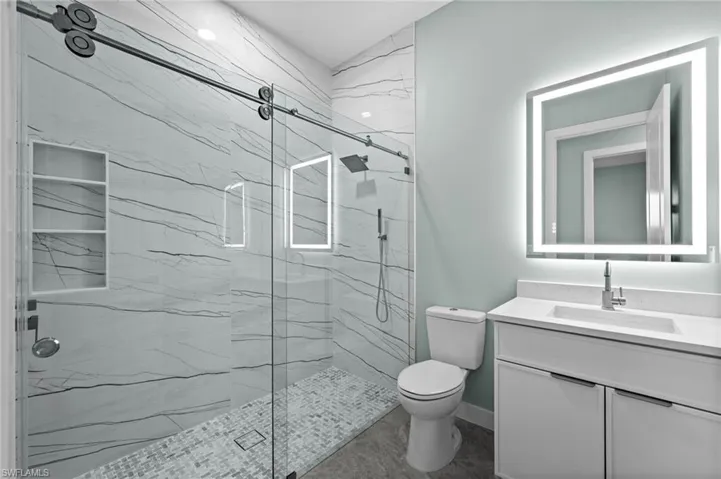Bathroom featuring a glass-enclosed shower with large format marble-look tile, built-in shower niches, and a mosaic tile shower pan