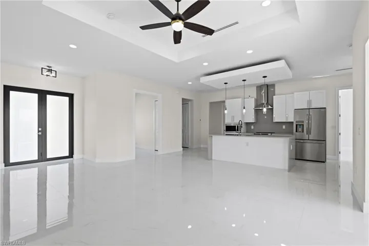 Kitchen with open floor plan, a raised ceiling, white cabinets, light marble finish flooring, and stainless steel refrigerator with ice dispenser