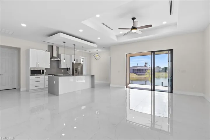 Kitchen featuring white cabinets, an island with sink, pendant lighting, open floor plan, and a tray ceiling