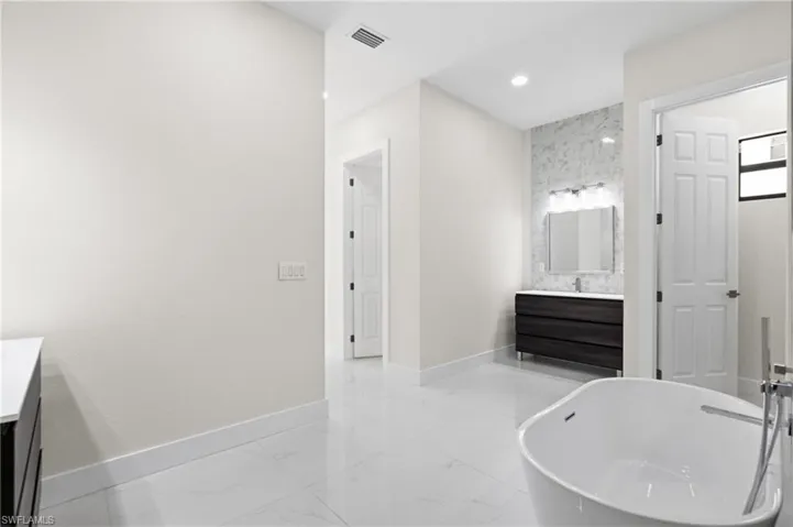 Bathroom featuring vanity, a freestanding tub, light marble finish flooring, and recessed lighting
